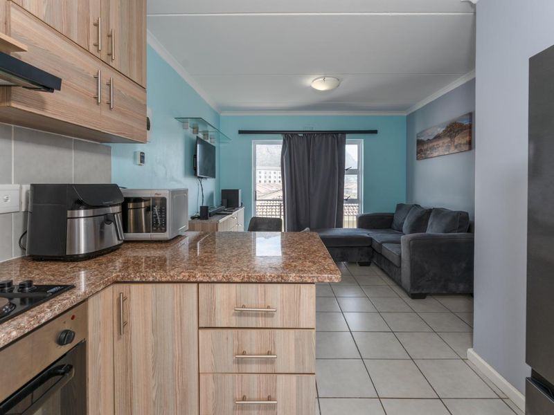Open-plan kitchen and living area featuring light wood cabinetry, granite countertops, tiled flooring, and direct access to a balcony through a sliding glass door.