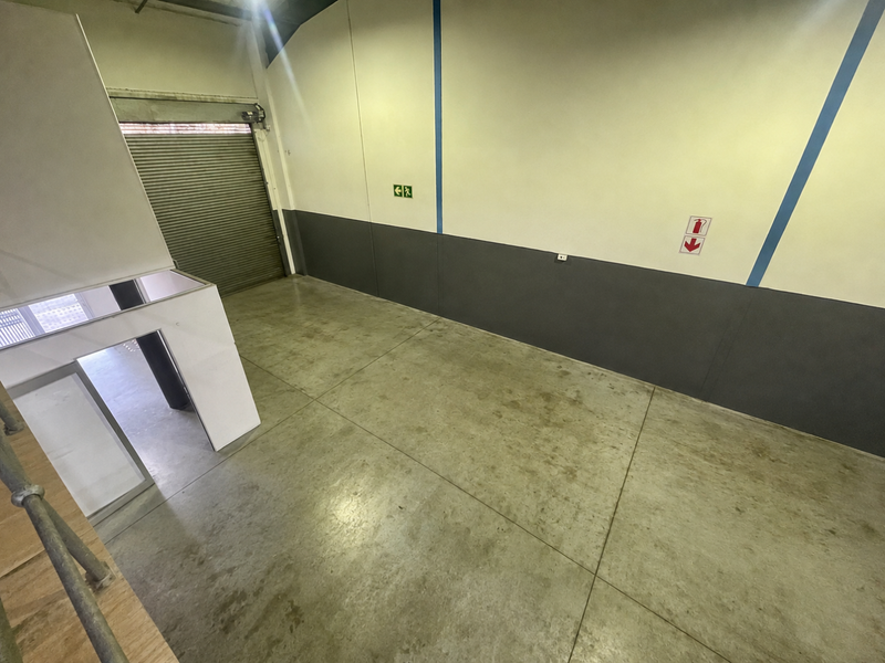 A spacious, empty industrial utility area featuring concrete flooring, a large roller shutter door, and fire safety signage.