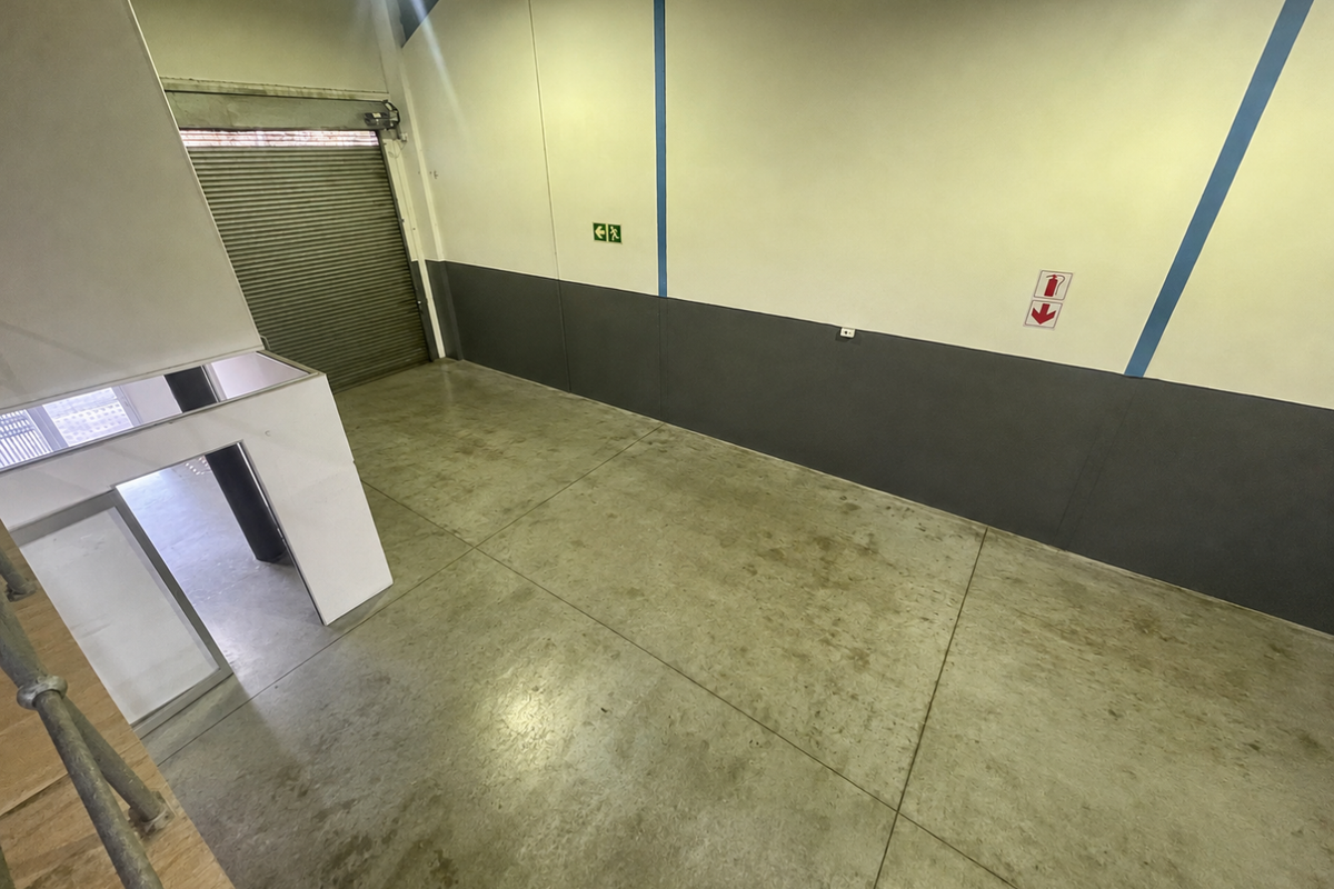 A spacious, empty industrial utility area featuring concrete flooring, a large roller shutter door, and fire safety signage.