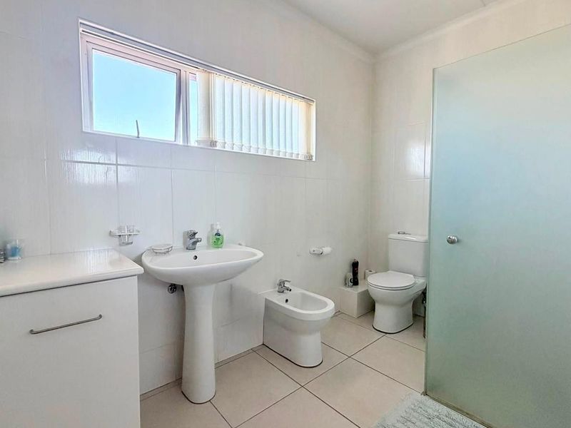 A functional bathroom featuring a pedestal basin, bidet, toilet, and a frosted glass shower enclosure with neutral tiled finishes.