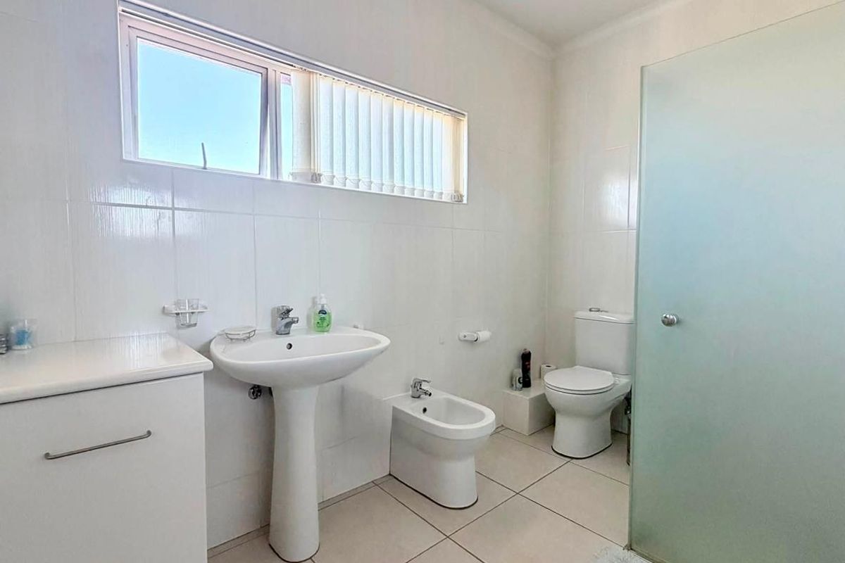 A functional bathroom featuring a pedestal basin, bidet, toilet, and a frosted glass shower enclosure with neutral tiled finishes.