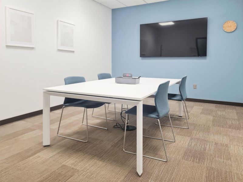 A modern, well-maintained office meeting room featuring neutral carpeted flooring, a blue accent wall, and a wall-mounted display screen.