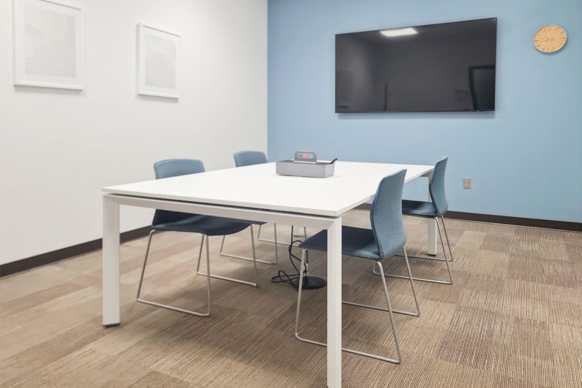 A modern, well-maintained office meeting room featuring neutral carpeted flooring, a blue accent wall, and a wall-mounted display screen.