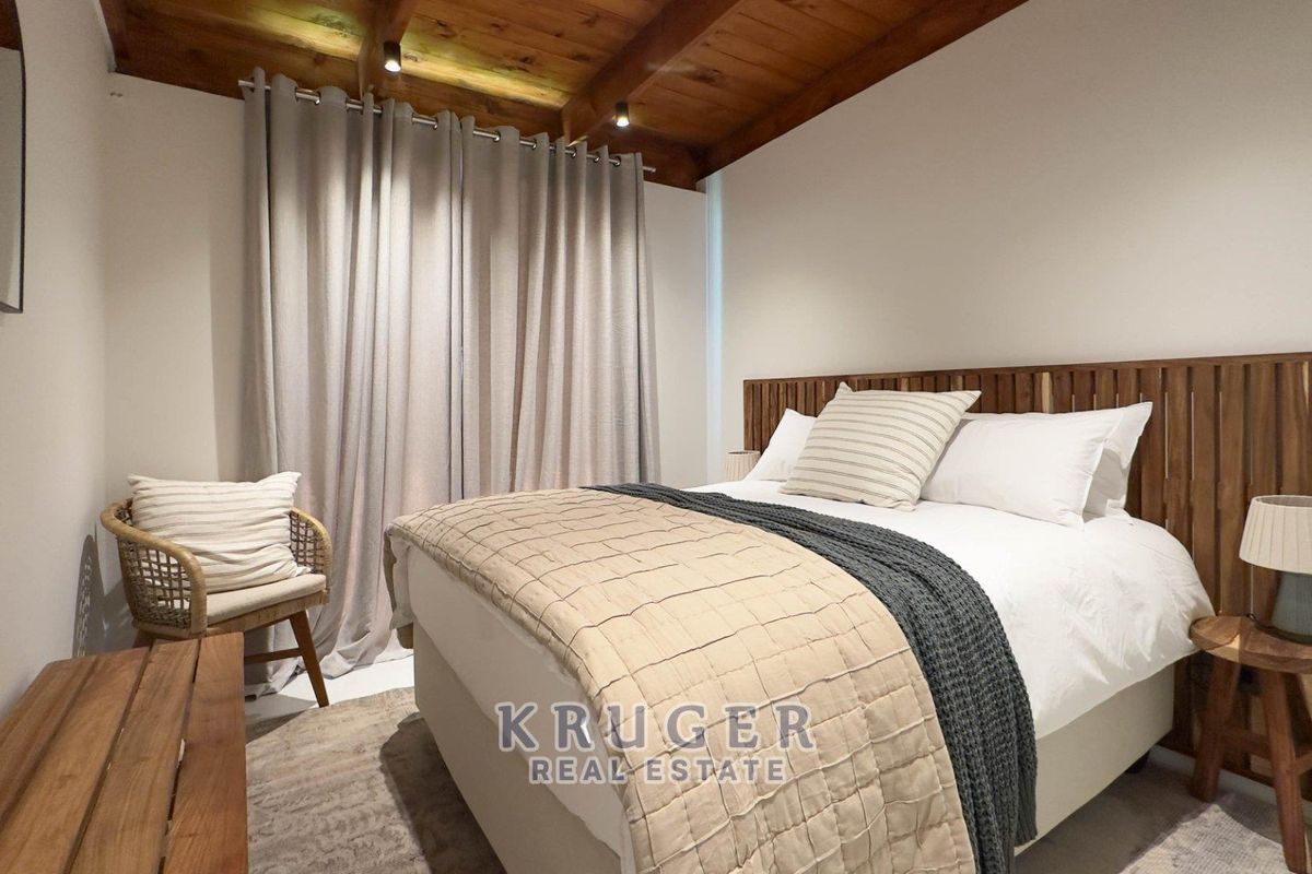 A cozy bedroom featuring exposed timber ceiling beams, recessed lighting, and a neutral color palette.