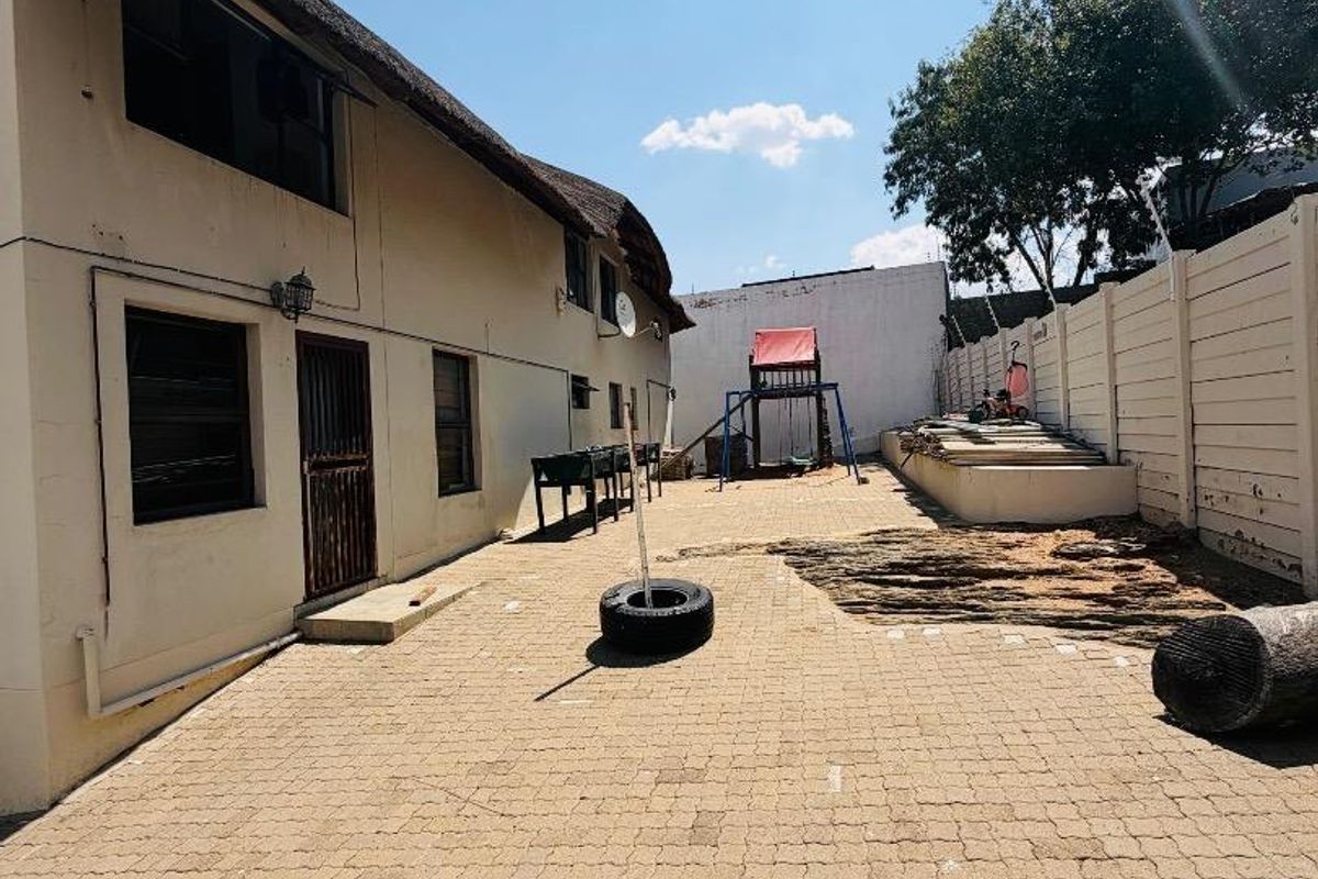 A spacious rear courtyard featuring paved flooring, a thatched roof building facade, and a secure precast concrete boundary wall.