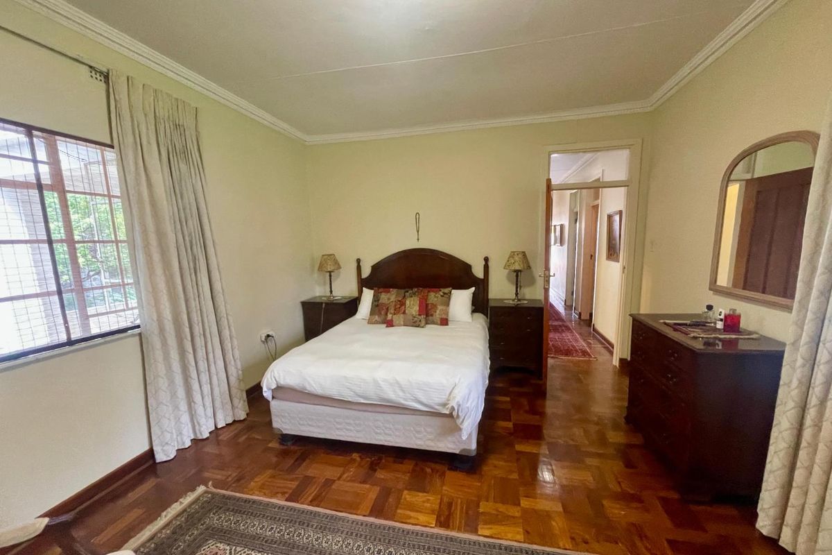 A well-proportioned bedroom featuring classic parquet flooring, large window with natural light, and direct access to the hallway.