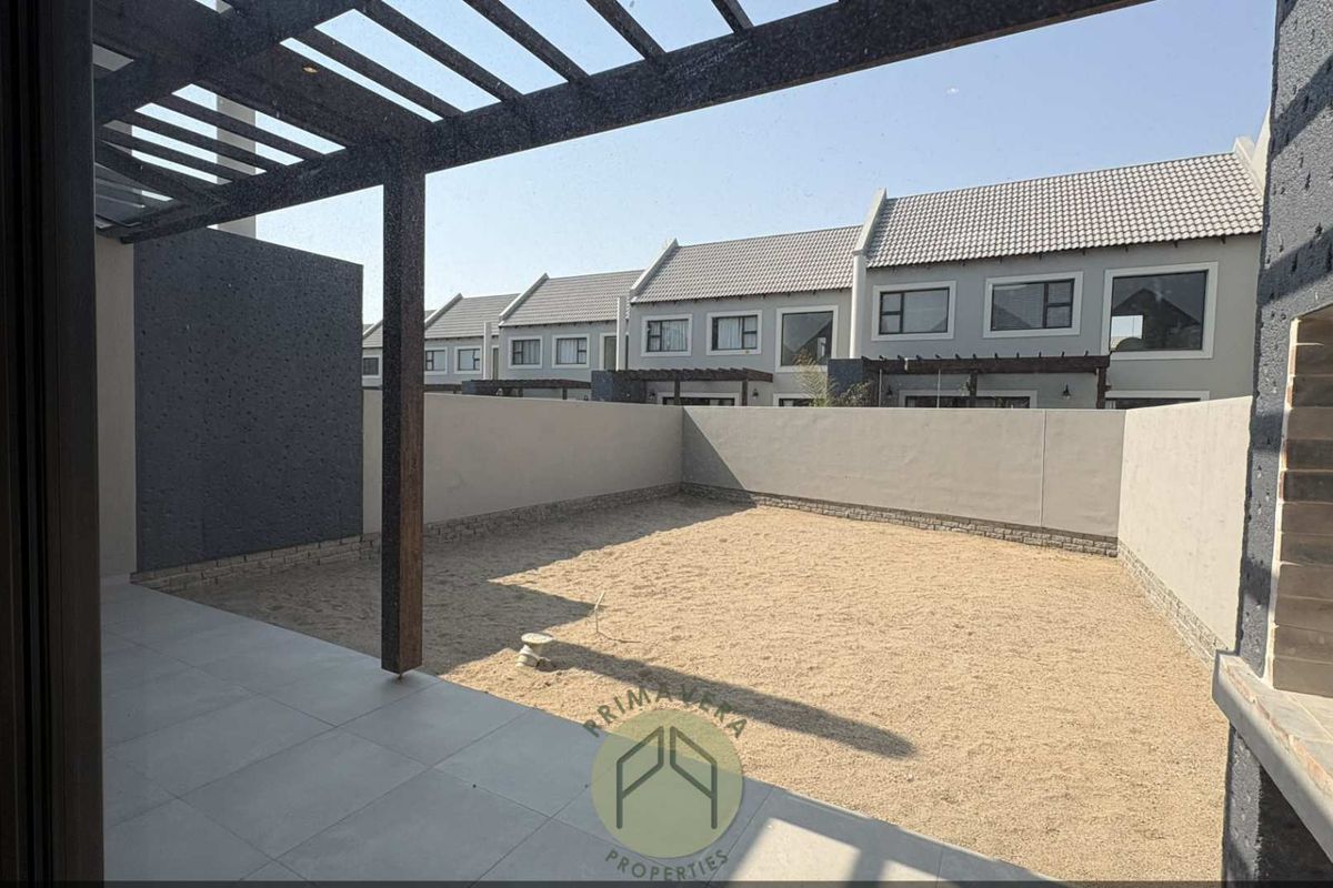 Rear garden area featuring a covered patio with a pergola, built-in braai, and a spacious, low-maintenance sandy yard enclosed by boundary walls.