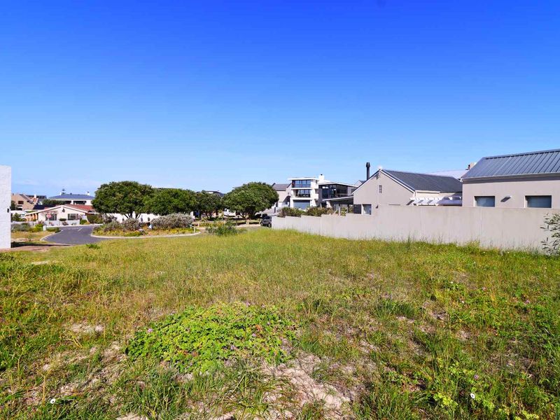 A vacant residential plot of land featuring natural grass cover and a boundary wall, situated in a developed neighborhood setting.