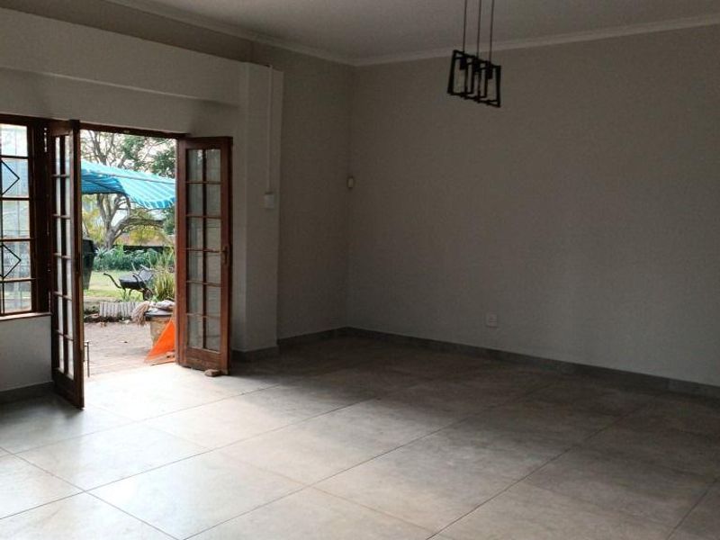 Spacious, empty living area featuring large format floor tiles, a modern pendant light, and double french doors opening to an outdoor patio space.