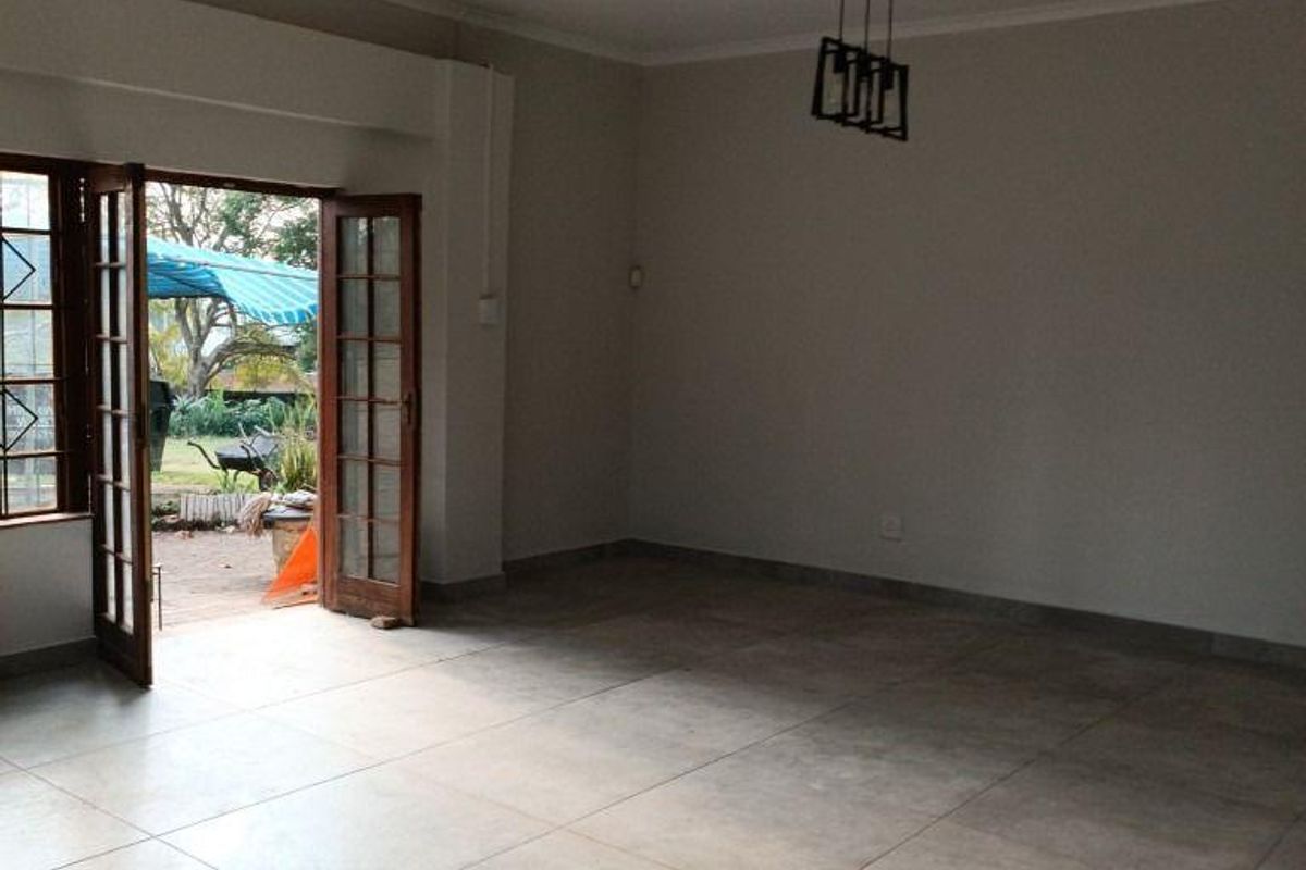 Spacious, empty living area featuring large format floor tiles, a modern pendant light, and double french doors opening to an outdoor patio space.