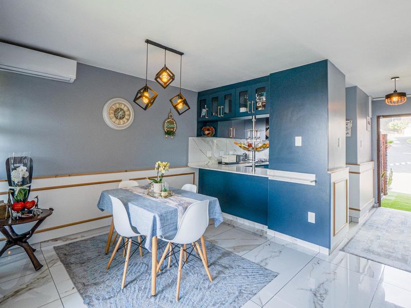 Open-plan dining and kitchen area featuring modern blue cabinetry, marble-look tiled flooring, wainscoting, and a split-system air conditioner.