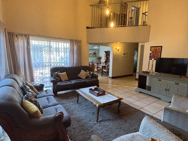 Spacious living room featuring a high vaulted timber ceiling, tiled flooring, and a mezzanine level overlooking the main area with access to a patio.