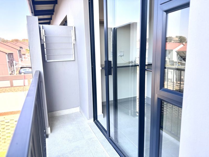 A clean, modern balcony featuring tiled flooring, a metal balustrade, and a wall-mounted drying rack, accessible via large sliding glass doors.