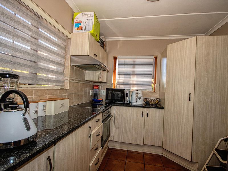 Compact kitchen featuring granite countertops, built-in oven, electric hob, extractor fan, and light wood-finish cabinetry with tiled flooring.