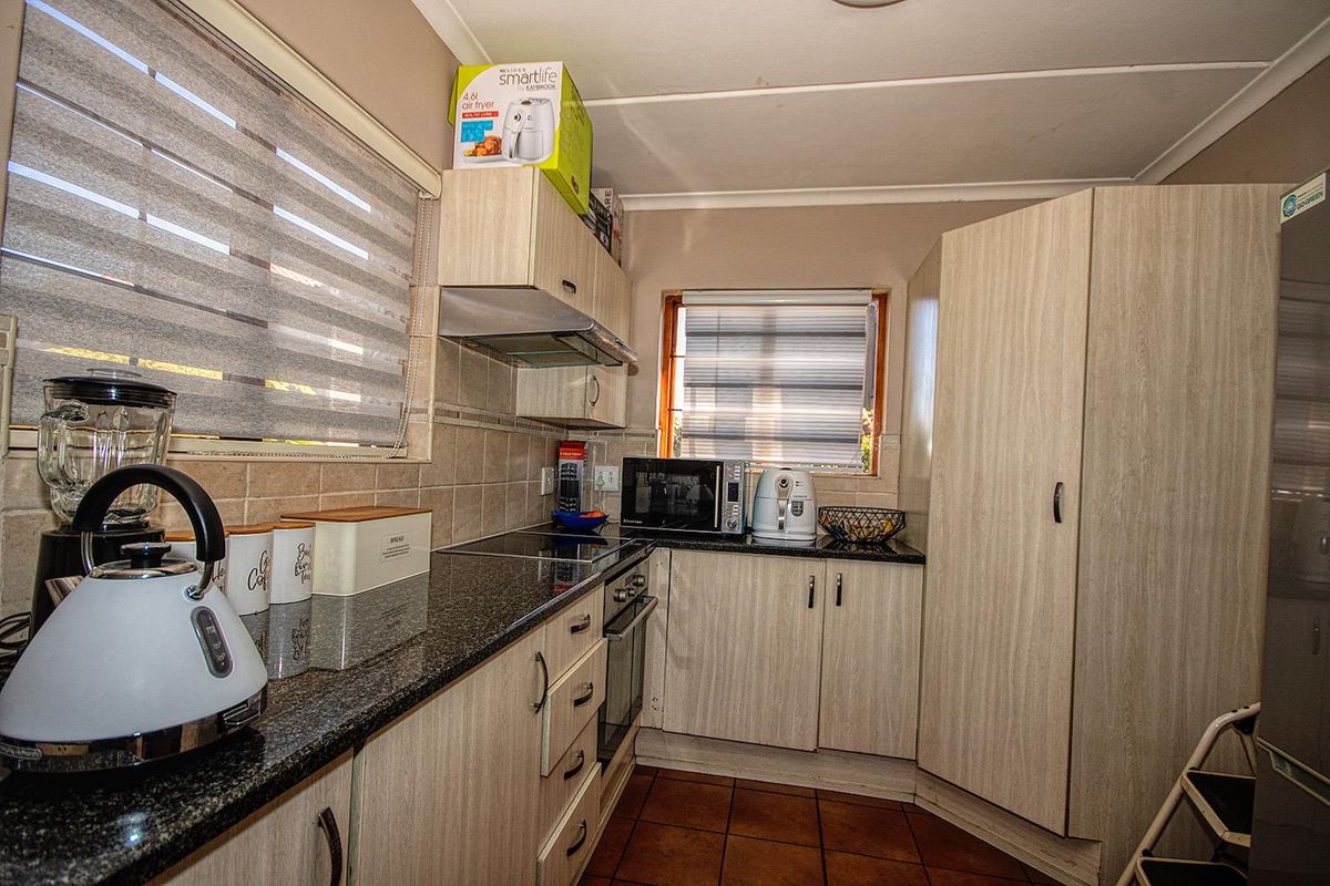 Compact kitchen featuring granite countertops, built-in oven, electric hob, extractor fan, and light wood-finish cabinetry with tiled flooring.