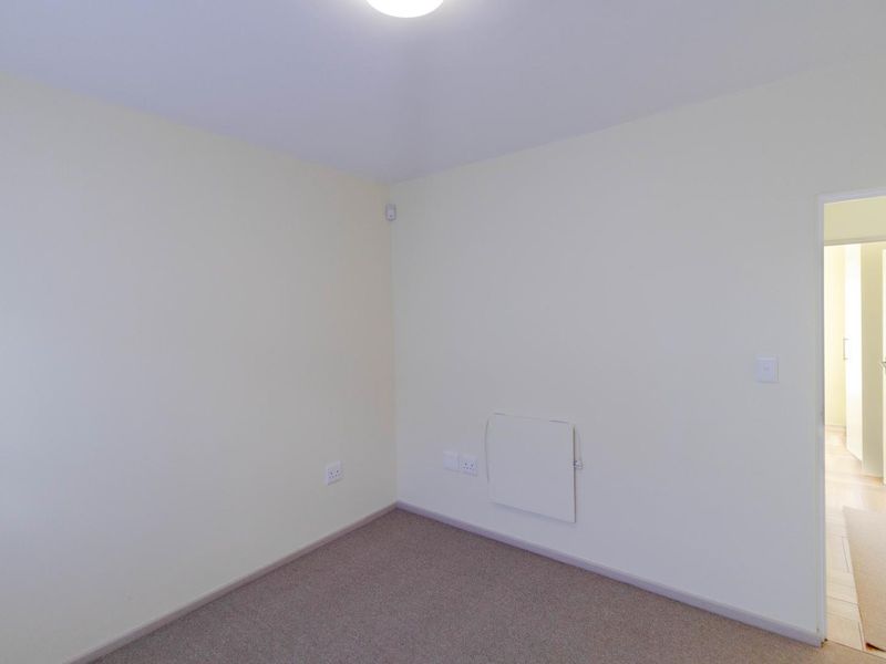 A clean, empty bedroom featuring neutral walls, carpeted flooring, and a standard internal door leading to an adjacent space.