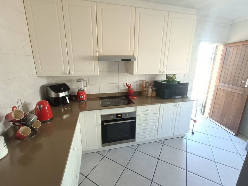 A functional kitchen featuring white cabinetry, stone countertops, integrated oven and hob, and tiled flooring with direct access to the exterior.