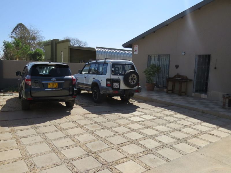 Front exterior view of the property featuring a paved driveway, tiled patio area, and secure entrance with security gates.