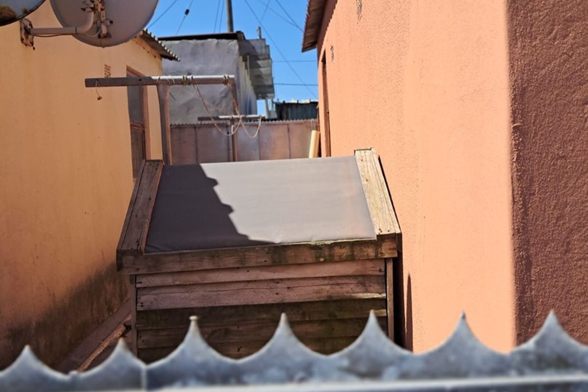 A narrow side passage of the property featuring plastered walls, satellite dishes, and security fencing.