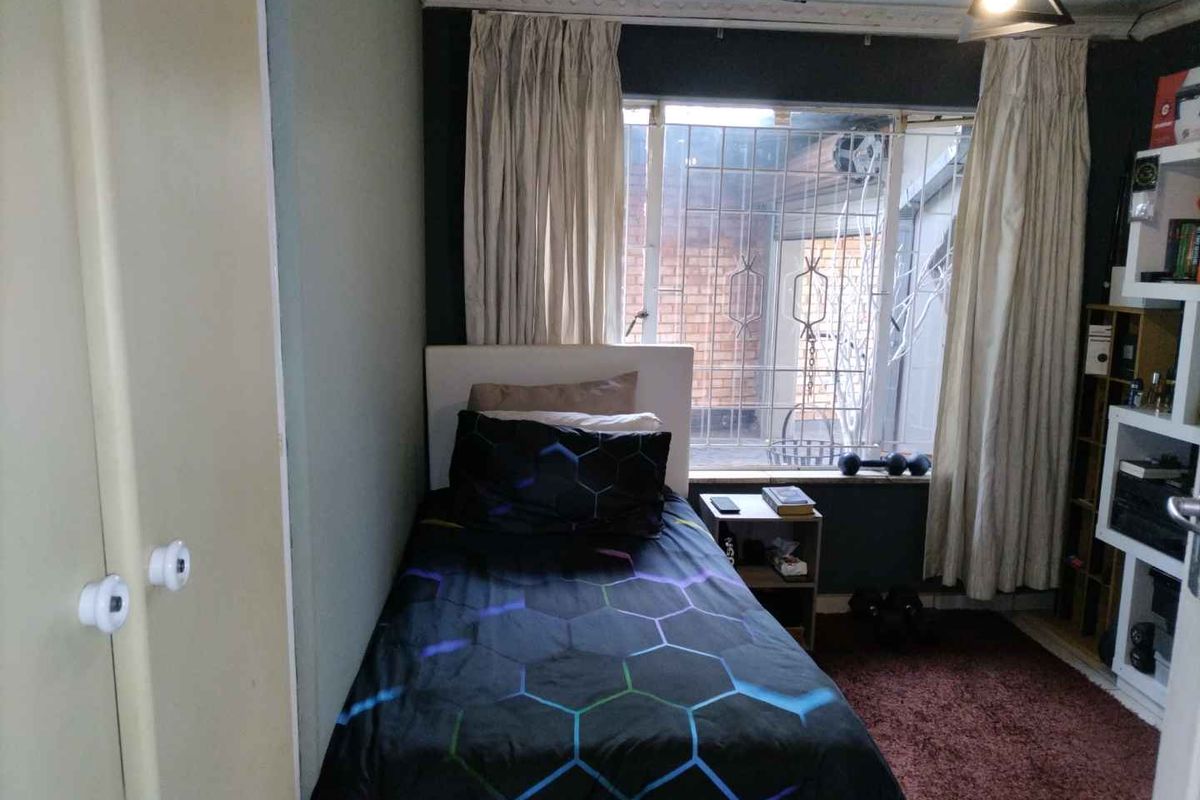 A compact bedroom featuring a built-in cupboard, security bars on the window, and decorative ceiling cornice.