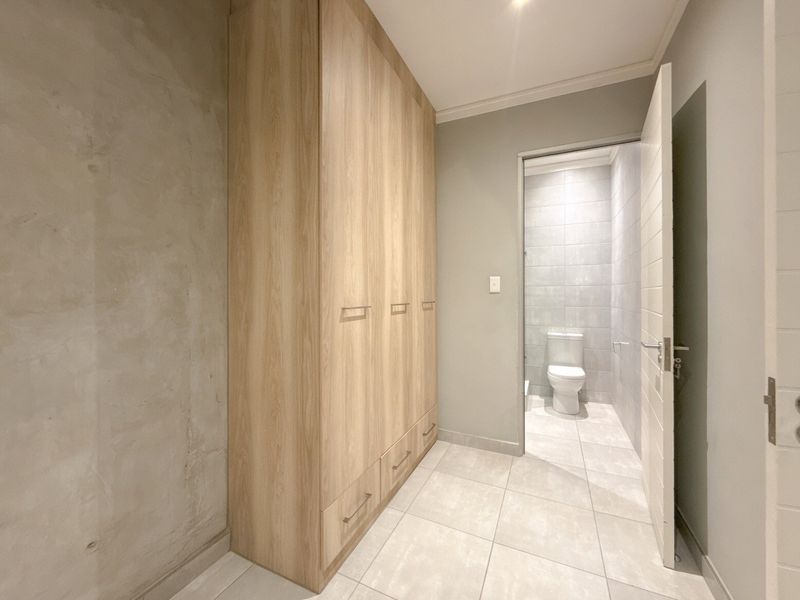 A modern bedroom area featuring built-in wooden wardrobes, neutral tiled flooring, and direct access to an en-suite bathroom.