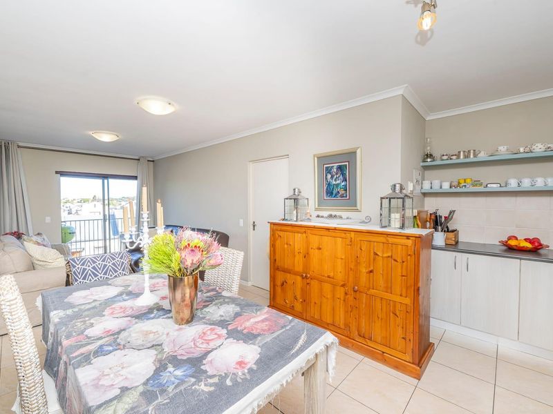 Open plan living and dining area featuring tiled floors, a compact kitchen with floating shelves, and sliding door access to a balcony.