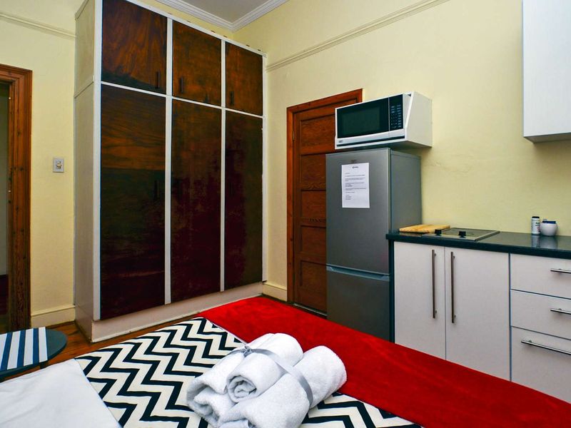A bedroom featuring a built-in wardrobe and a compact kitchenette area with cabinetry and a hob.