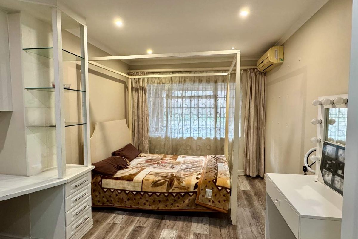 A bedroom featuring wood-look laminate flooring, recessed ceiling lighting, a built-in shelving unit, and a wall-mounted air conditioning unit.