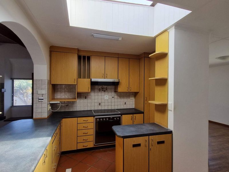 A functional kitchen featuring built-in wooden cabinetry, laminate countertops, a built-in oven with hob, and a skylight providing natural light.