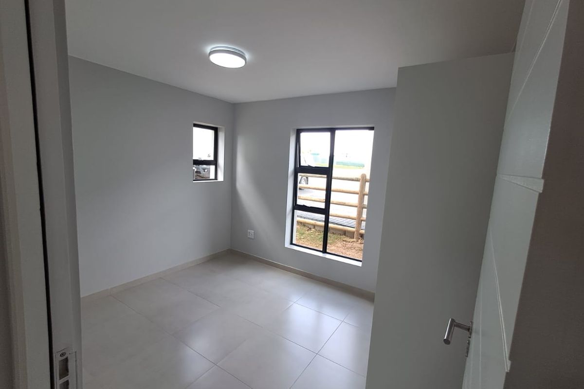 A bright, empty bedroom featuring neutral tiled flooring, modern black-framed windows, and a clean, minimalist aesthetic ready for personalization.