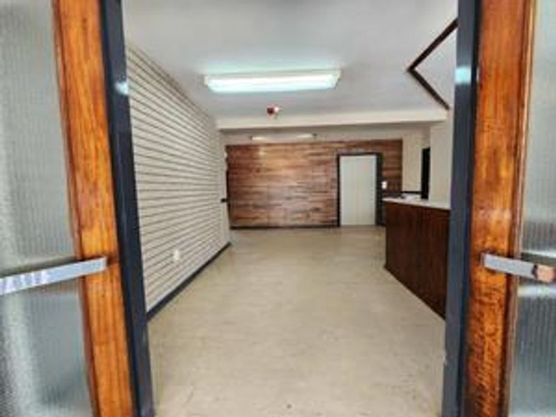 An empty entrance or reception area featuring slatwall paneling, wood-look wall accents, and a built-in counter, presenting a dated commercial aesthetic.
