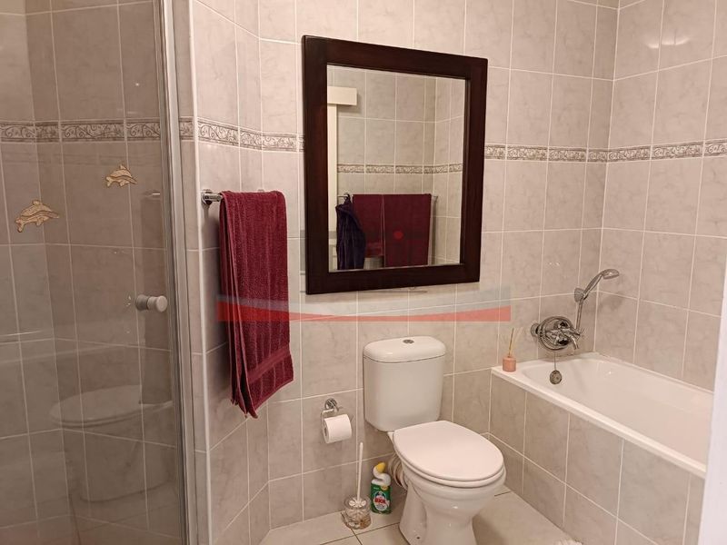 A functional bathroom featuring a shower enclosure, bathtub, toilet, and wall-mounted mirror with neutral wall tiling.