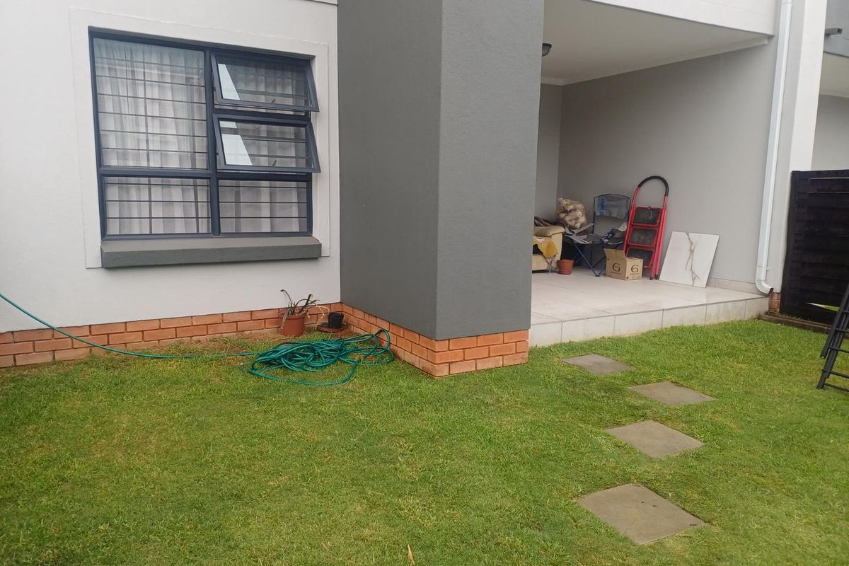 A view of the rear exterior featuring a covered patio area, tiled flooring, and a small private garden with paved stepping stones.