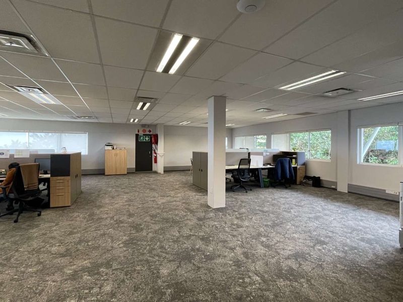 Open-plan office space featuring a suspended ceiling, recessed lighting, carpeted flooring, and built-in workstation partitions.