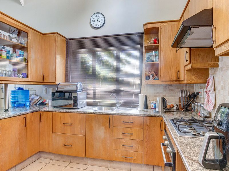 A functional kitchen featuring wooden cabinetry, granite countertops, a gas hob, built-in oven, and tiled backsplash with a window for natural light.