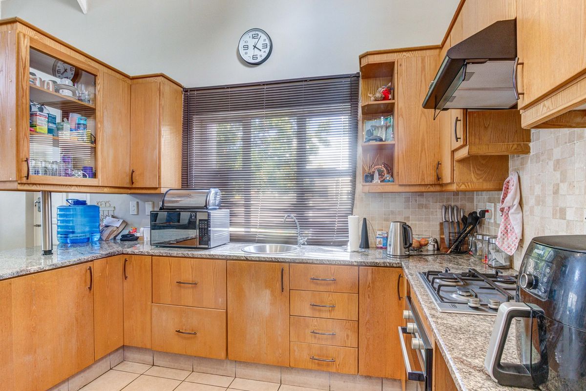 A functional kitchen featuring wooden cabinetry, granite countertops, a gas hob, built-in oven, and tiled backsplash with a window for natural light.