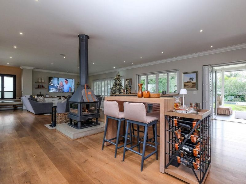 Spacious open-plan living area featuring high-quality timber flooring, a central freestanding fireplace, and seamless access to the outdoor patio through large sliding glass doors.