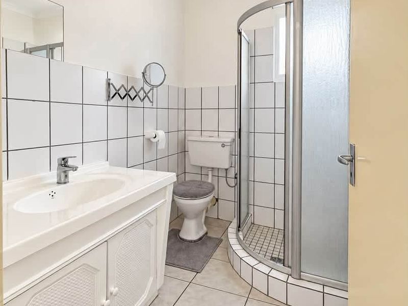 A functional bathroom featuring a corner shower enclosure, a vanity cabinet with a basin, and classic white wall tiling.