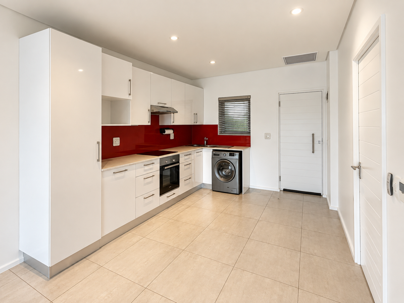 Modern kitchen featuring white high-gloss cabinetry, a striking red glass splashback, integrated appliances, and neutral tiled flooring in an open-plan layout.