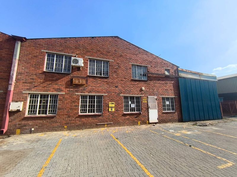 Front elevation of an industrial brick building featuring steel-framed windows, a paved parking area, and corrugated metal side cladding.