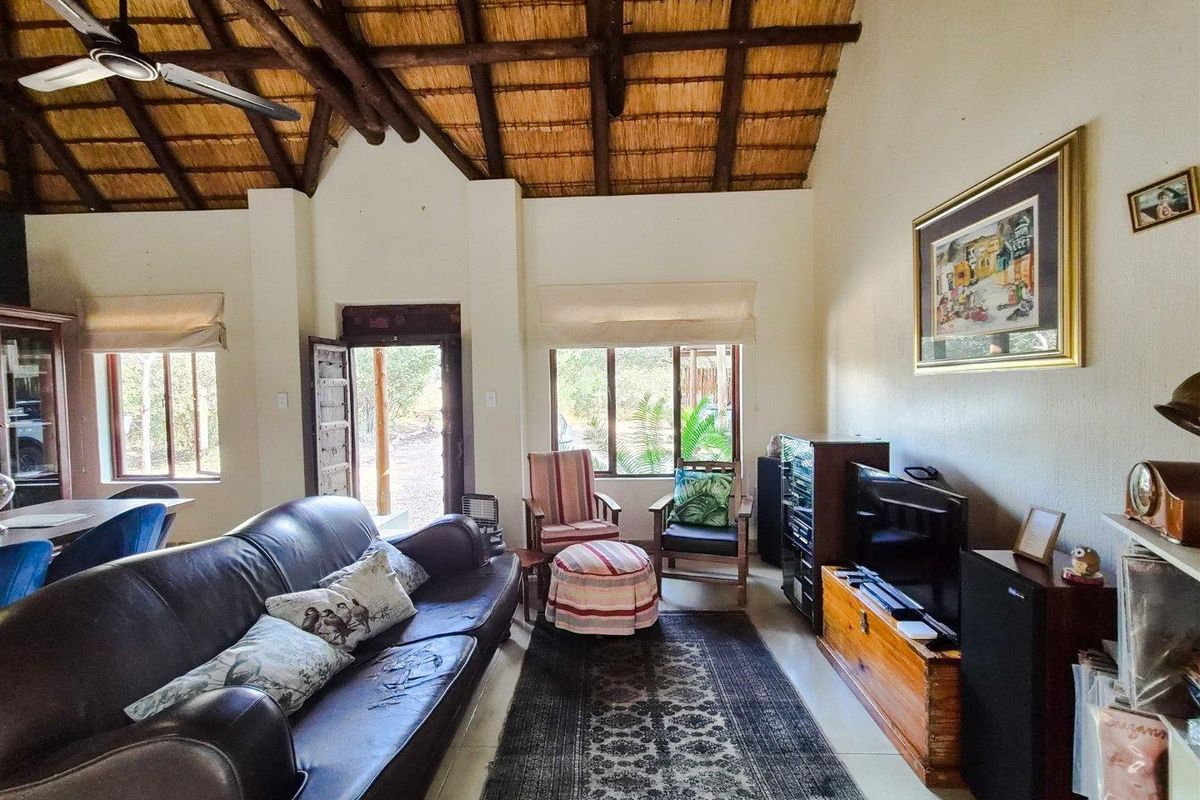 Spacious living room featuring a high vaulted thatched ceiling with exposed timber rafters, tiled flooring, and direct access to the exterior.