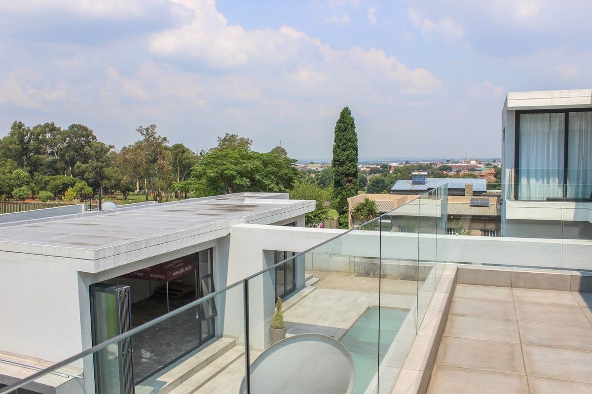 Elevated view of a modern property featuring a flat roof, glass balustrades, and a swimming pool area with surrounding landscape.