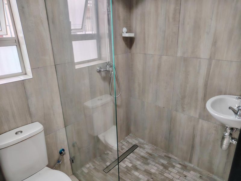 A modern bathroom featuring wood-look wall tiles, a glass shower enclosure with a linear drain, a wall-mounted basin, and a ceramic toilet.