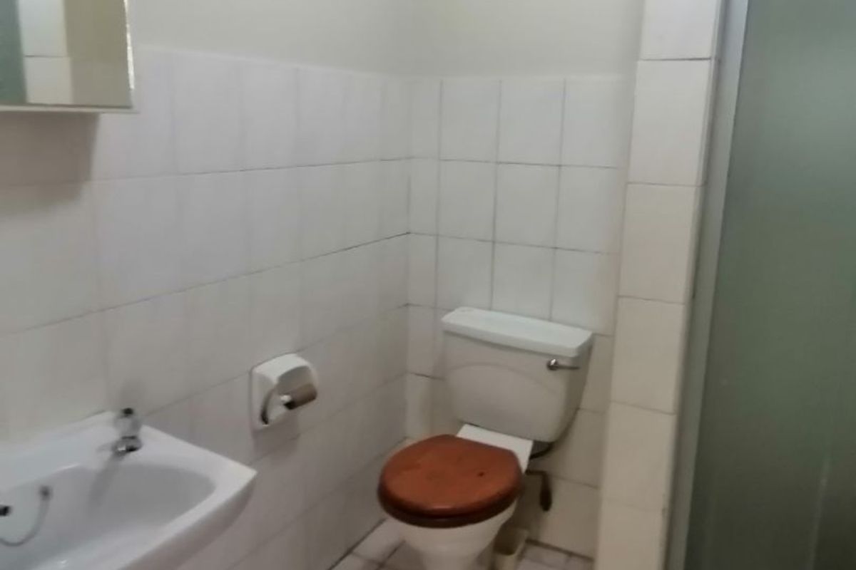 A functional bathroom featuring a pedestal basin, a standard toilet, and a shower enclosure with tiled walls and flooring.