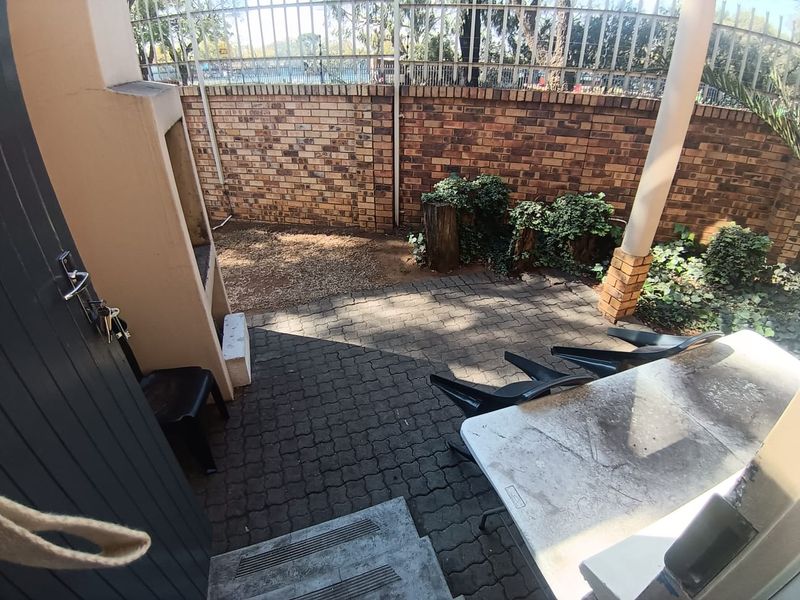 A private outdoor patio area featuring paved flooring, a built-in braai, and a brick boundary wall with security fencing.