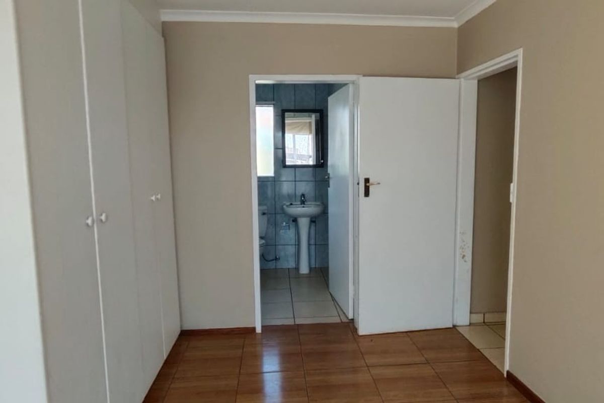 A vacant bedroom featuring built-in cupboards, tiled flooring, and direct access to an en-suite bathroom.