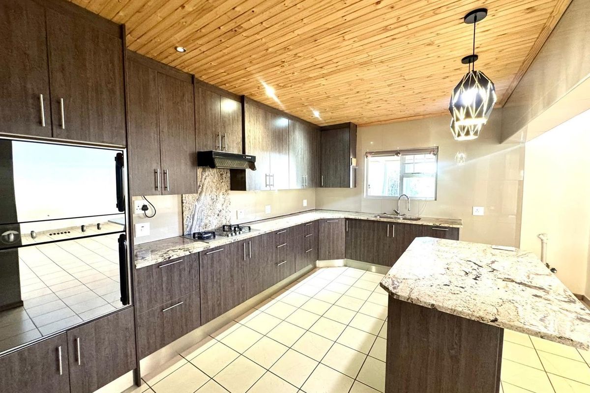 Modern kitchen featuring dark wood cabinetry, granite countertops, a central island, built-in oven, gas hob, and a distinctive timber-clad ceiling.