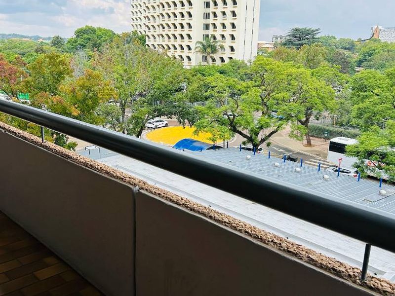 A balcony featuring a metal railing and tiled flooring, offering an elevated urban view of the surrounding neighborhood and nearby high-rise buildings.