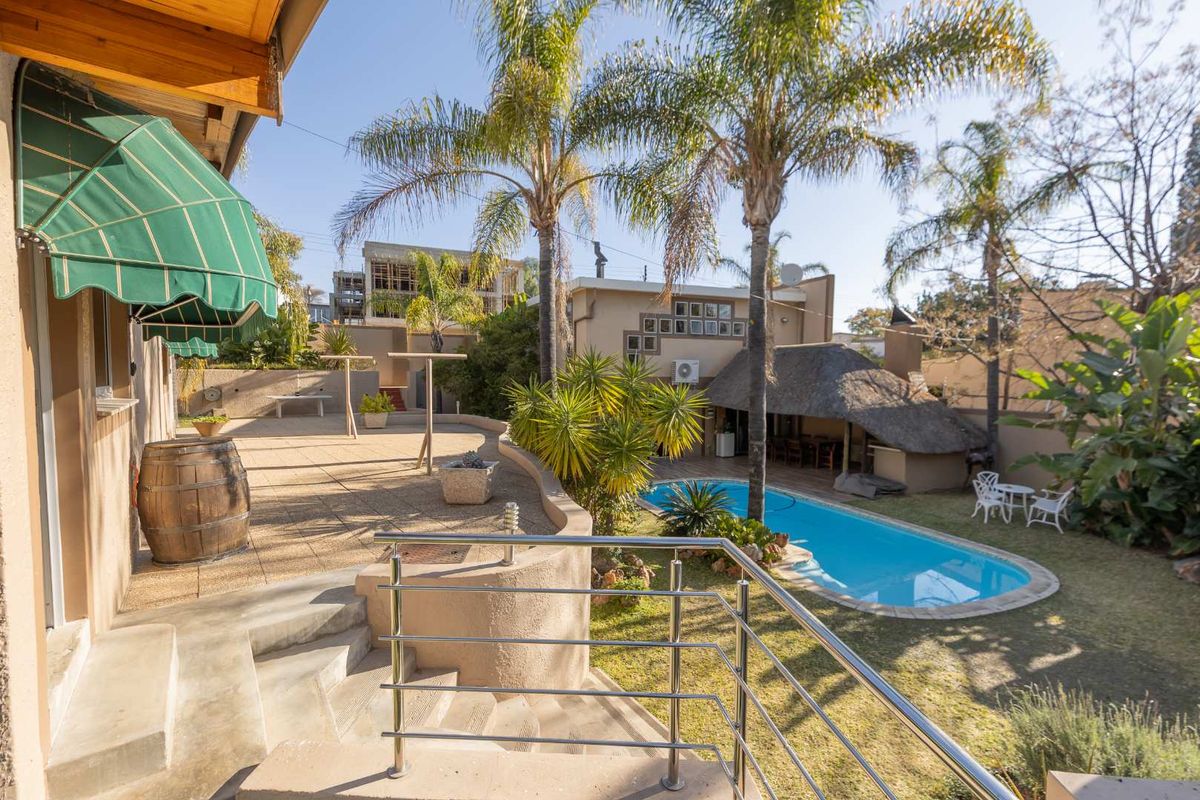 Spacious rear garden featuring a swimming pool, a traditional thatched lapa, and a paved patio area with stainless steel balustrades.