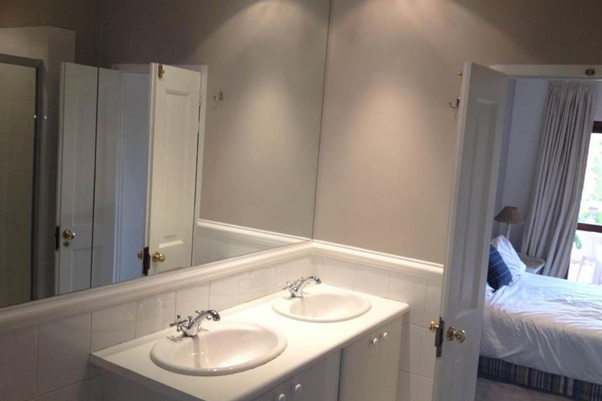 A functional bathroom featuring a double vanity with integrated sinks, tiled splashbacks, and a large wall mirror.